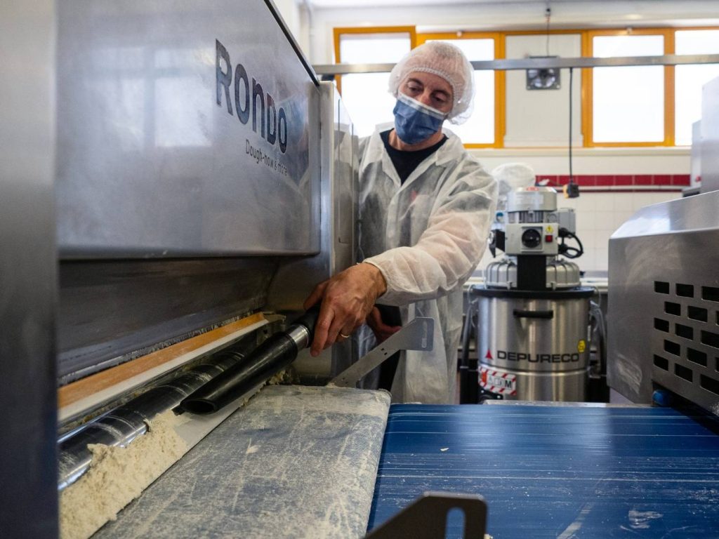 Food production employee using an industrial vacuum to recover spilled flour powder from processing equipment and a conveyor area