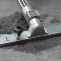M100 JC industrial vacuum floor tool collecting dust and granular debris from a concrete floor.