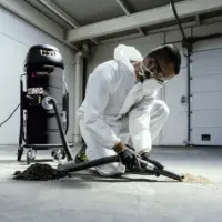 Operator uses a Depureco MINIBULL industrial vacuum to collect fine powder and dark production debris from a concrete floor.