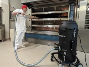 Bakery worker uses the Depureco XM20 OVEN vacuum with a long cleaning wand inside a commercial deck oven.