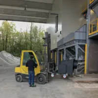 Forklift positioning a mobile tiltable pre-separator beneath bulk material processing hoppers at an industrial facility.