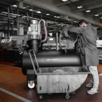 Operator empties separated metal chips and swarf from the RAM OIL 500 T sump vacuum into a collection bin.