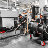 Operator uses a RAM OIL 500 T sump vacuum to remove coolant, metal chips, and sludge from a CNC machine tank.