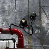 Operator uses the M PRO industrial vacuum to clean dust from elevated process piping in a manufacturing facility.