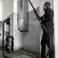 Operator uses the M PRO industrial vacuum with an extension wand to clean dust from elevated ventilation ductwork.