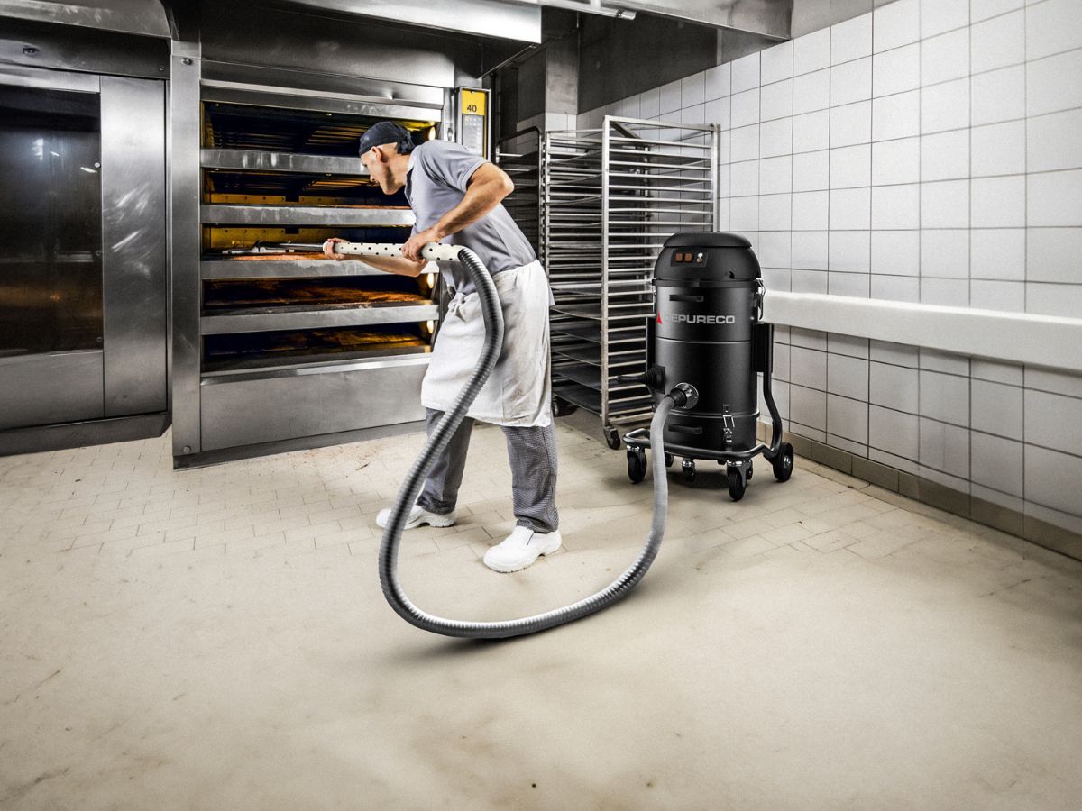 Worker cleaning bakery floor using Depureco industrial vacuum near ovens