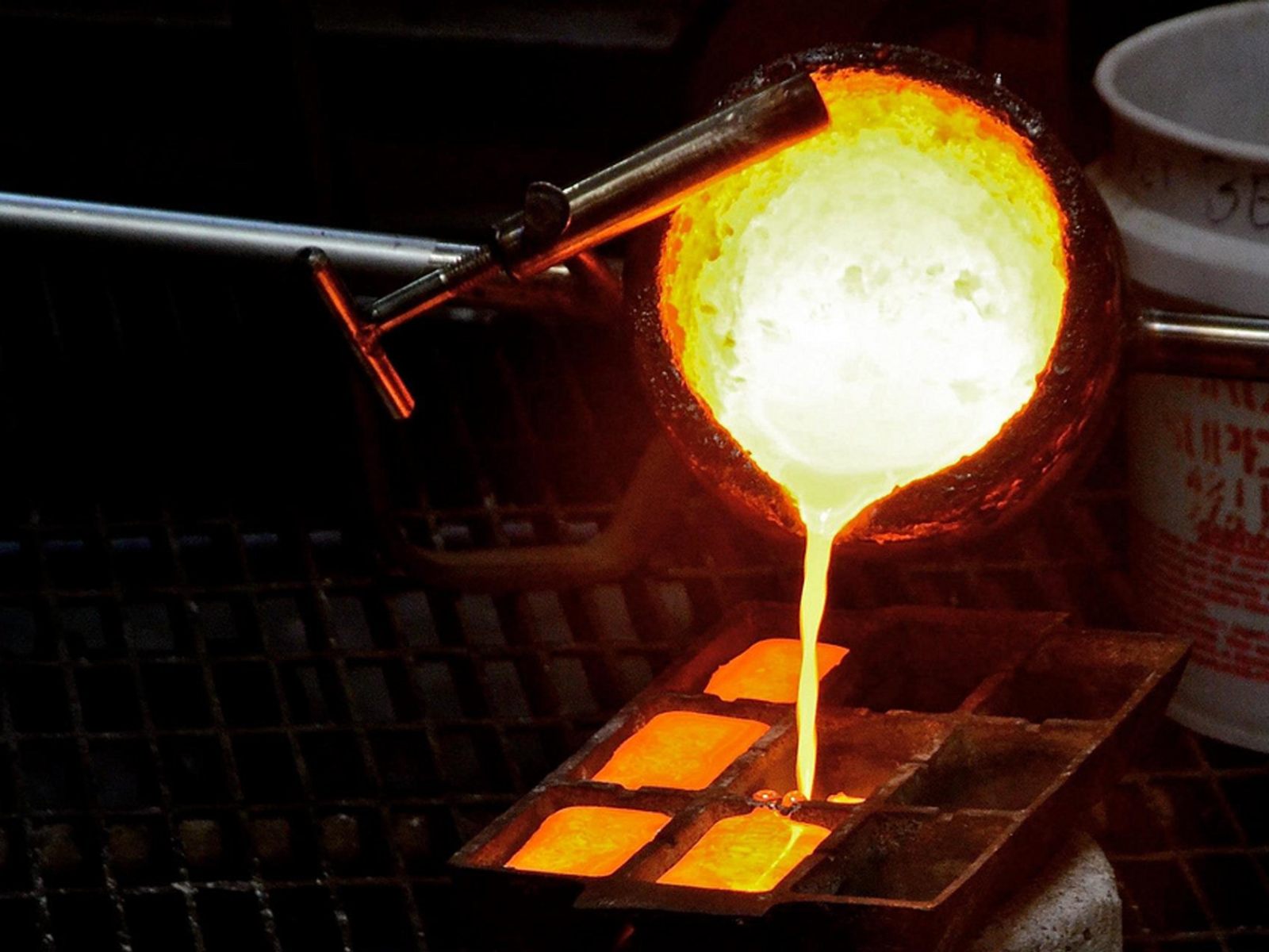 Molten metal being poured from crucible into multi-cavity mold in foundry